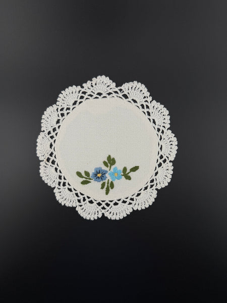 Handmade white cotton crochet coaster with blue embroidered flowers and lace edging
