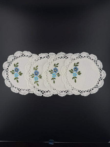 Set of four handmade white cotton crochet coasters with blue floral embroidery
