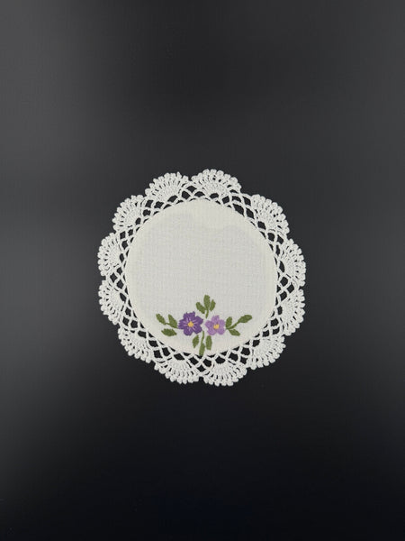 Handmade white cotton crochet coaster with purple embroidered flowers and lace edging