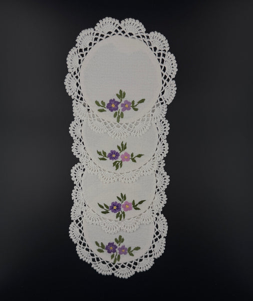 Set of four handmade white cotton crochet coasters with purple floral embroidery